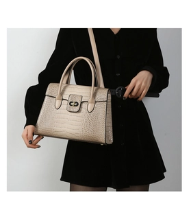 Detail of beige crocodile pattern handbag with metal rotating clasp on black dress