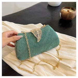 Detailed macro view of the emerald green clutch with a golden leaf clasp and fine chain