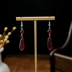 Macro detail of red teardrop beaded earrings on a gold display stand with retro style