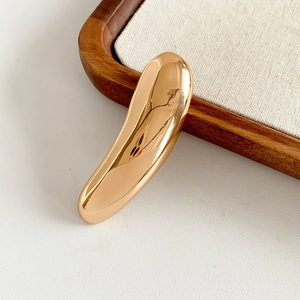 Detail of minimalist gold-finish long metallic brooch on an elegant jewelry display tray