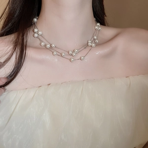 Detail of layered silver chain necklace with elegant white pearls on model's neck