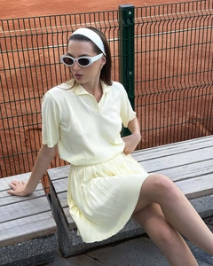 Detail von hellgelbem Strick-Poloshirt und passendem Faltenrock an einem Model im Freien