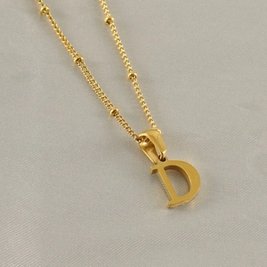 Close-up of golden letter D pendant with beaded chain on a grey textured background