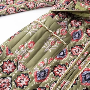 Detail of green floral quilted jacket showing intricate gold-white woven trim and pocket texture