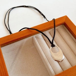 Close-up of a silver hollow oval pendant with black cord in a wooden jewelry box