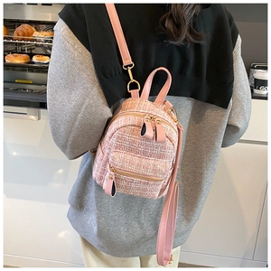 Pink tweed mini backpack with gold zippers shown on a model in a cozy kitchen setting