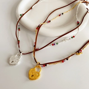 Close-up of heart lock pendants with embossed patterns and colorful beads on leather cords