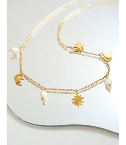 Detalle del collar dorado con estrellas, luna y perlas de agua dulce sobre espejo