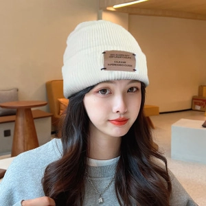 Detail of a white winter knit beanie showing the texture and brown leather patch