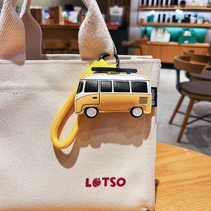 Cute yellow leather bus keychain bag charm with black metal hook on a canvas tote bag