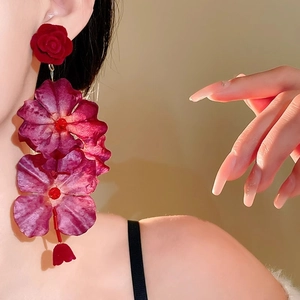 Dettaglio macro di orecchini a rosa in tessuto rosso con petali a cascata su modella