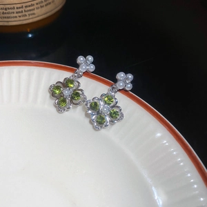 Detailed macro shot of clover-shaped earrings with green stones and pearls on ceramic plate