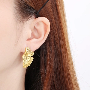 Close-up of golden ginkgo leaf earrings with fine brushed texture on a female model