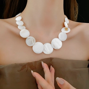 Close-up of bohemian geometric white shell necklace worn by model on a dark background