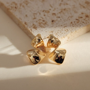 Macro view of minimalist golden twisted geometric square stud earrings on stone texture