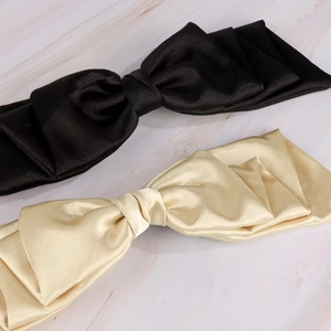 Detailed view of elegant satin bow hair clips in black and champagne on marble surface