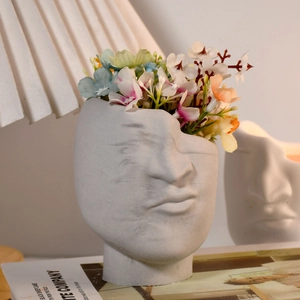 Artistic face-shaped concrete planter with colorful flowers in a minimalist home setting