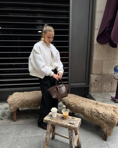 Street style view of a white fleece bomber jacket styled with black trousers and leather bag