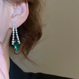 Detailed view of silver diamond-encrusted earrings with emerald marquise-cut gemstone