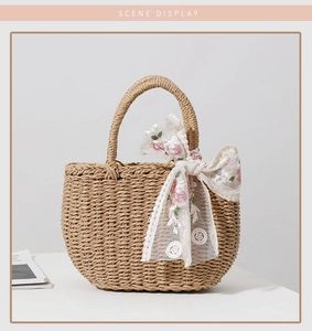 Detailed close-up of straw handbag featuring white lace bow and pink floral embroidery
