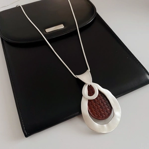 Close-up of a silver teardrop pendant with brown woven texture on a sleek snake chain