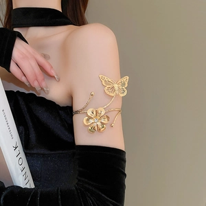 Detail of a golden metal arm cuff featuring hollow butterfly and flower designs on a model