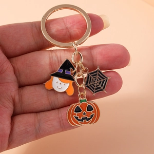 Detail of Halloween keychain with enamel pumpkin, witch and spider web charms held in hand