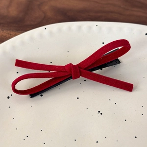 Close-up of a red suede bow hair clip on a decorative ceramic plate with a dark wood background