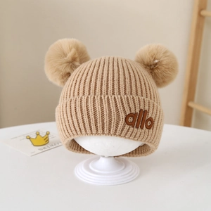 Detail der gerippten Baby-Strickmütze mit zwei Bommeln und allo Stickerei-Akzent
