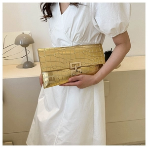 Fashionable golden envelope clutch with crocodile texture shown on a white dress