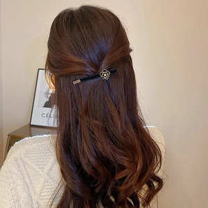 Detail of black velvet hair clip with a gold-trimmed camellia flower on brown hair