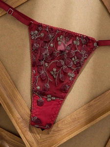 Détail d'un string T-back rouge foncé avec broderie florale dorée et mesh