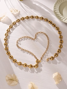 Dettaglio di un set di gioielli dorati con maglie circolari e catena a cuore su bianco