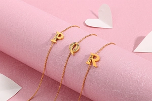 Macro view of gold-plated P, Q, R letter charms with diamonds on a pink surface