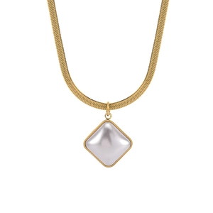 Macro detail of golden necklace featuring a white shell pearl pendant and sleek snake chain
