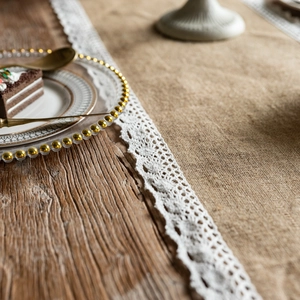 Detail of natural jute table runner with white lace trim and fringe on a rustic wooden table