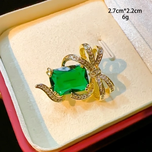 Détail de la broche émeraude avec nœud doré présentée dans un coffret cadeau