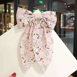 Detailed close-up of a pink floral bow hair clip with long ribbons on a display card