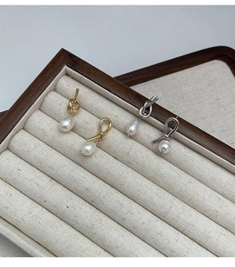 Detailed view of gold and silver knotted earrings with pearls in a wooden jewelry box