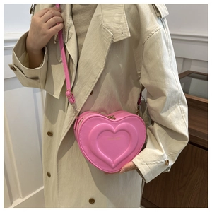 Detailed view of a pink heart-shaped crossbody bag with gold hardware and logo engraving