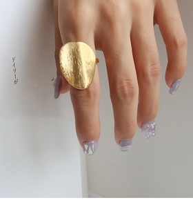 Close-up of golden oval ring with brushed matte texture on model's hand with book