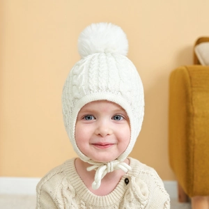 Beige cable knit baby winter hat with large faux fur pom and secure chin straps