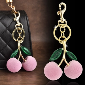 Pink velvet cherry keychain with glitter green leaf and gold clasp on a black bag
