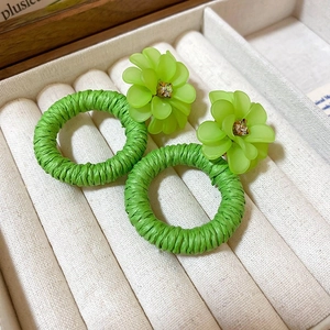 Macro detail of green woven flower stud earrings with acrylic petals and crystals