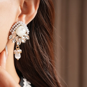 Dettaglio di orecchini vintage con perle e diamanti indossati da una modella con gocce d'oro
