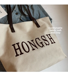 Detail of canvas tote bag showing brown leather handles and HONGSH letter print logo
