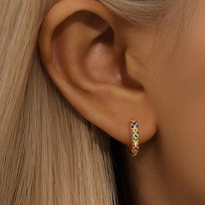 Close-up of luxury gold huggie hoops featuring rainbow gemstones on a female model