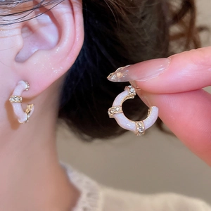 Close-up of gold-plated C-shaped bamboo stud earrings with pink enamel and crystals