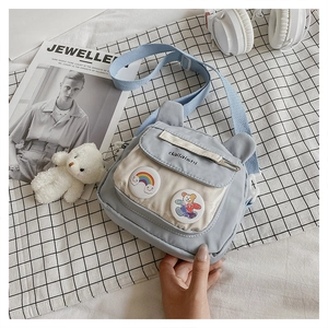 Detail of light blue canvas shoulder bag with cute bear badges on checkered fabric