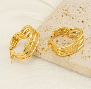 Gros plan de boucles d'oreilles cœur dorées multicouches sur une surface en pierre